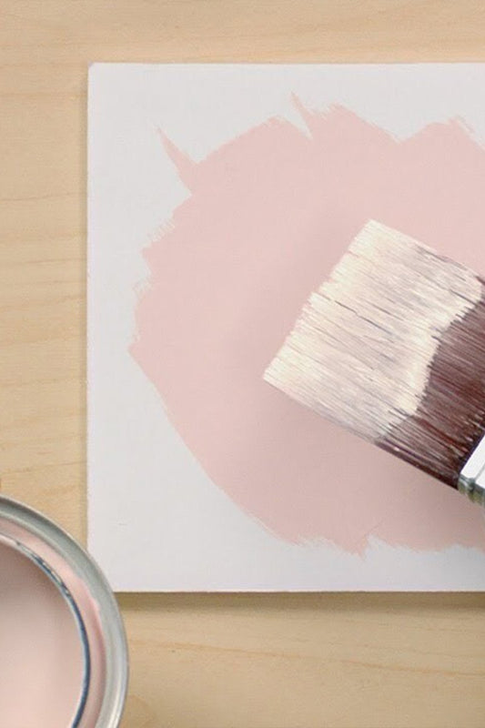 top down view of paint can with pink paint and hand holding paint brush above white block with painted pink circle